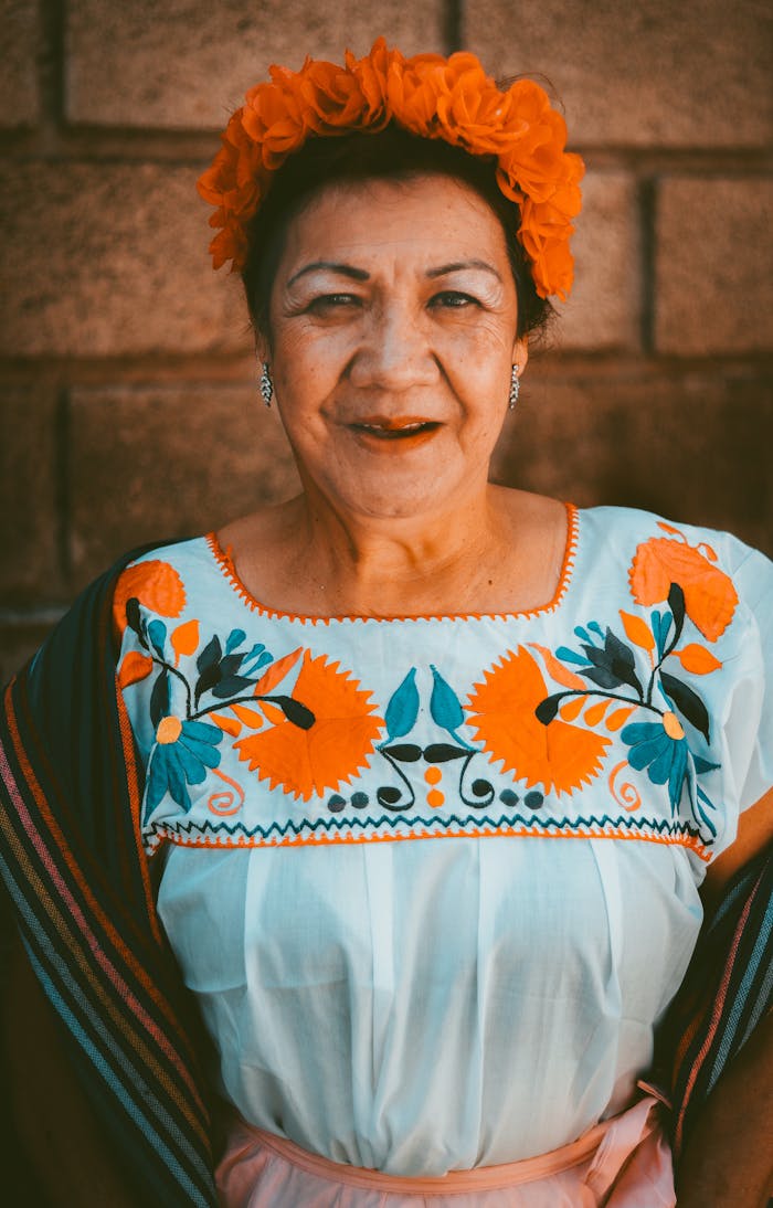 Smiling woman in traditional Mexican attire with floral headdress and embroidery.