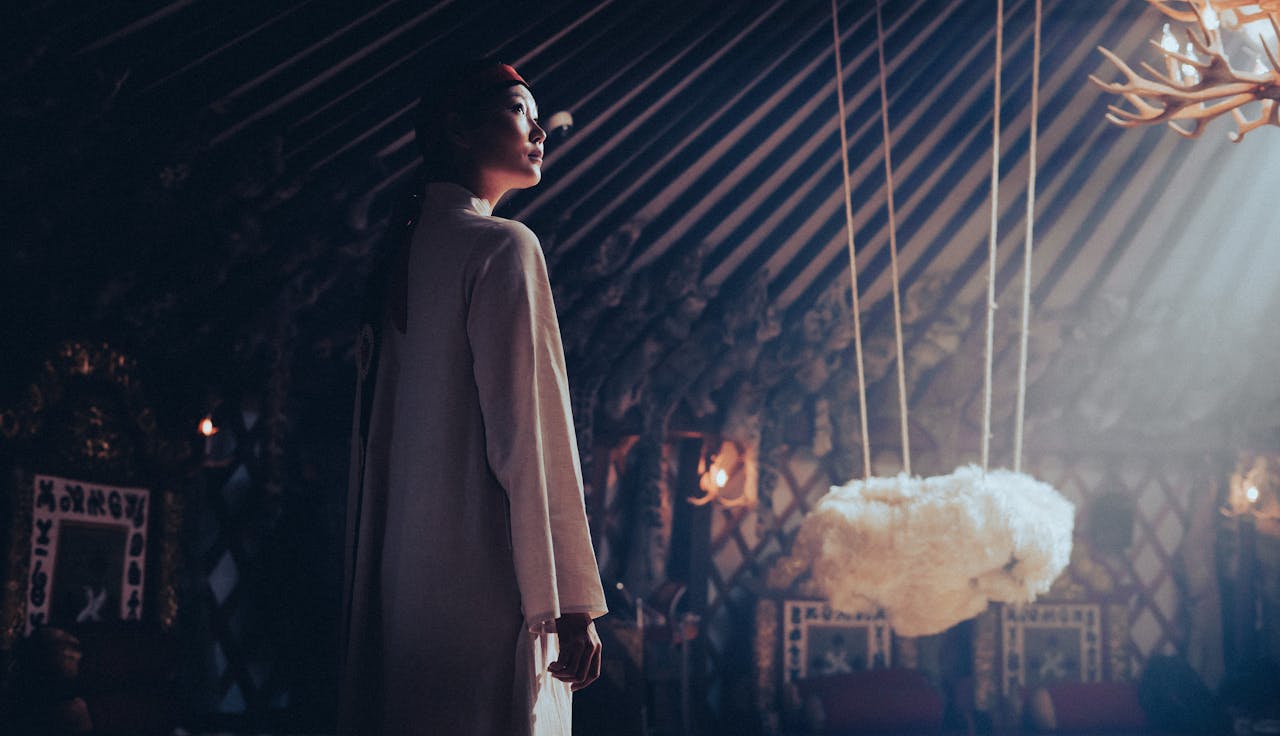 services-01 A woman in traditional attire stands inside a beautifully decorated Mongolian yurt.
